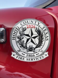 Hood County, Texas Fire Services emblem on a red vehicle, featuring a star, oak, and palm, with the years 1866 and 2026 displayed.